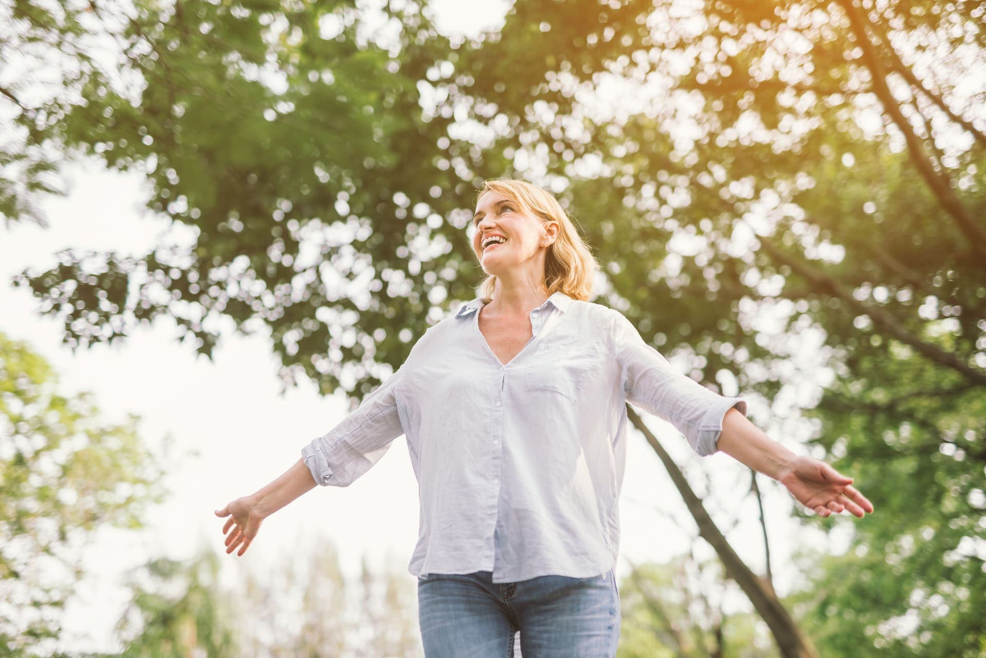 A woman standing outdoors among trees in the sunlight